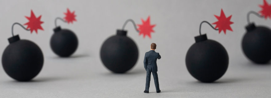 Miniature business figure facing a field of cartoon bombs